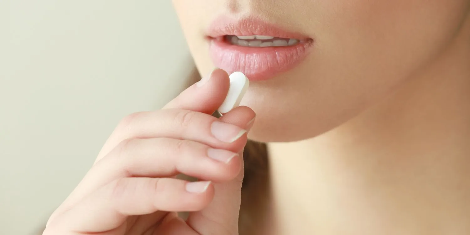 Close up of woman holding an amino acid supplement tablet to her open mouth.