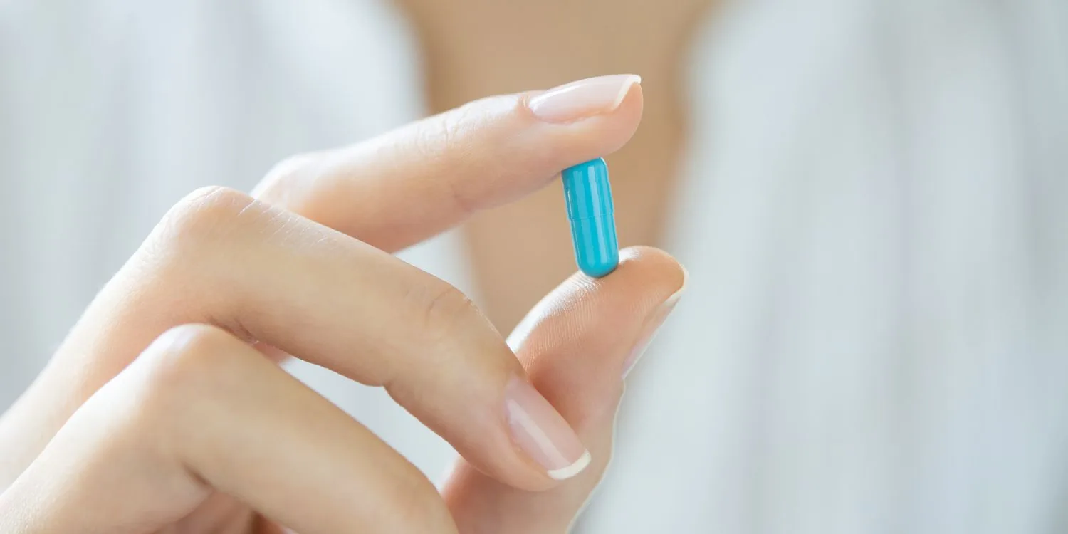 A closeup of a person holding a blue capsule between their thumb and forefinger.