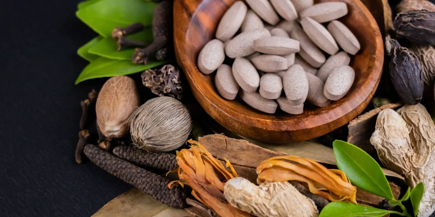 Brownish tablet supplements in a bowl surrounded by natural ingredients.